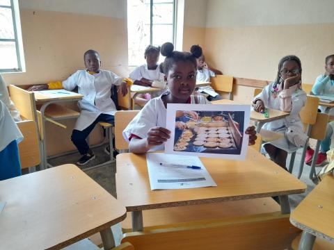 Menina segurando uma foto com panquecas durante a sessão do Diálogos da Nutrição em uma escola no sul de Angola.